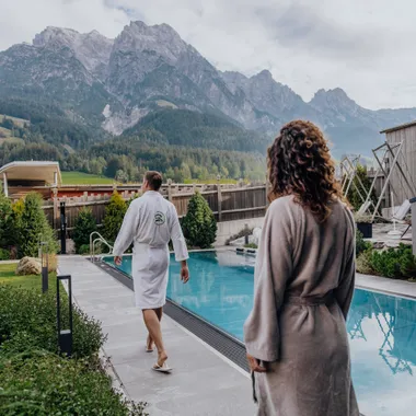 Herbstzauber & Wellnesstage Paar im Bademantel geht am Außenpool eines Wellnesshotels in den Alpen entlang
